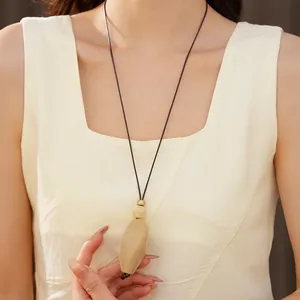 Gros plan d'un pendentif style bois sur un long collier porté par un mannequin asiatique.