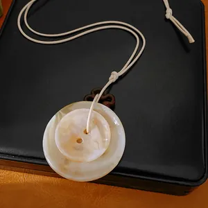 Vue détaillée du pendentif en forme de bouton en acrylique crème sur un cordon fin