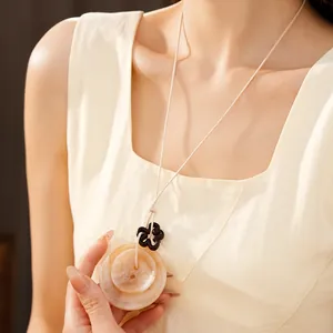 Vue détaillée d'un collier ethnique en acrylique avec pendentif fleur et cordon beige.