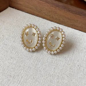 Macro detail of 14k gold plated smiley face earrings with pearls and cat eye stone.