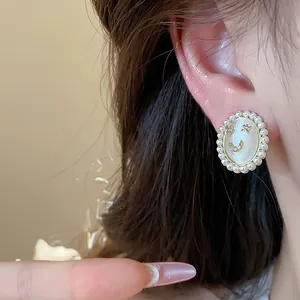 Close-up of 14k gold plated smiley face earring with cat-eye stone and pearl border