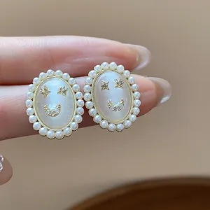 Detailed view of 14k gold plated cat eye stone and pearl smiley face stud earrings