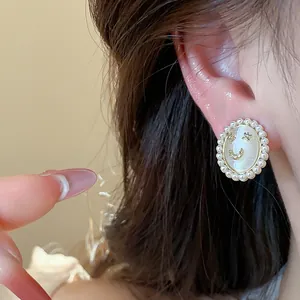 Close-up of 14K gold plated cat-eye stud earring with pearl border and smiley face