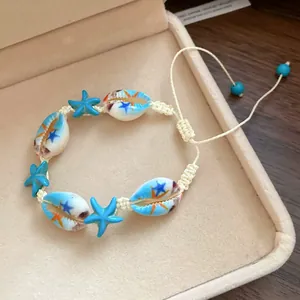 Close-up of hand-woven bracelet with painted cowrie shells and blue starfish charms