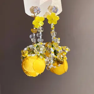 Détail de boucles d'oreilles de vacances avec fleurs en tissu jaunes, perles et zircons.