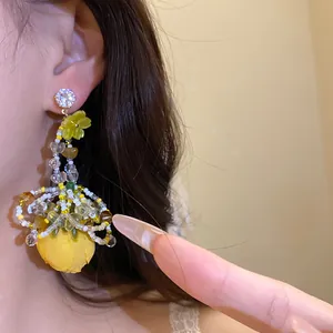Gros plan de boucles d'oreilles pendantes style vacances avec fleur en tissu jaune et zircon.