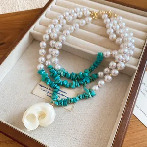 Detail of multi-layer pearl necklace with turquoise chips and a spiral shell pendant