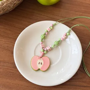 Close-up of a pink ceramic apple necklace with beaded green woven cord on a white plate.