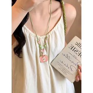Detailed view of handmade pink ceramic apple pendant necklace with woven green cord