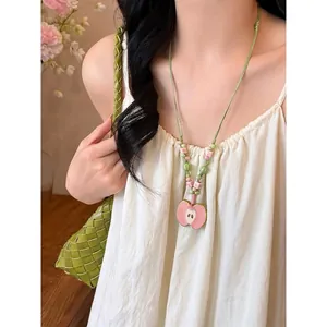 Close-up detail of a pink ceramic apple pendant beaded necklace worn on a white summer dress