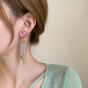 Detailed shot of long dangling earrings featuring a pink heart and colorful crushed stones.