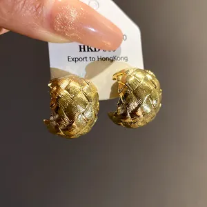 Gros plan de boucles d'oreilles dorées en forme de C avec une texture tressée complexe.