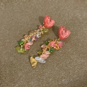 Close-up of colorful heart-shaped stone tassel earrings with vibrant multi-gem details