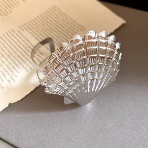 Vista detallada de un brazalete de metal plateado pulido con diseño de concha marina.