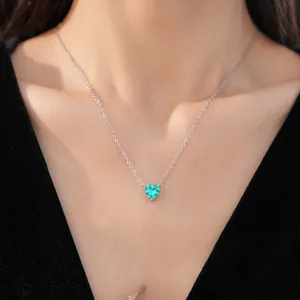 Detail of a minimalist silver necklace with a heart-shaped green zircon on a model.