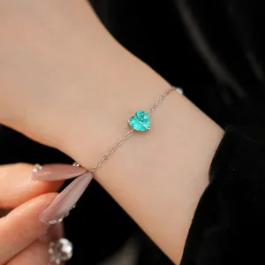 Close-up of a delicate silver bracelet with a heart-shaped green zircon on a wrist.