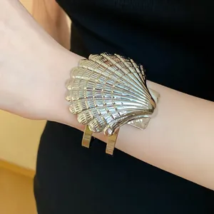 Elegante brazalete abierto de metal con forma de concha y un acabado dorado en la muñeca