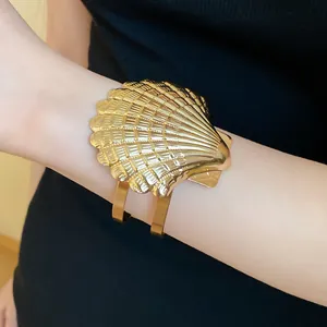 Vista detallada de un brazalete de metal dorado vintage con forma de concha en brazo