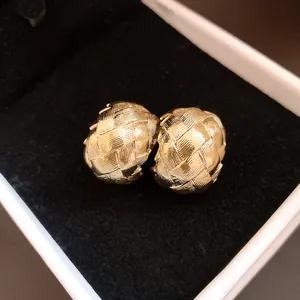 Vue détaillée de boucles d'oreilles dorées en forme de C avec un motif tissé vintage.