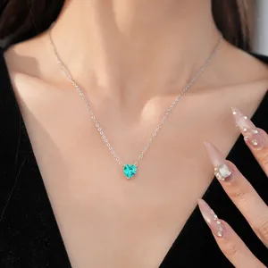 Close-up detail shot of a dainty heart-shaped green zircon pendant necklace on a model