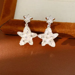 Dettaglio di orecchini a stella con intarsio in conchiglia bianca e strass.