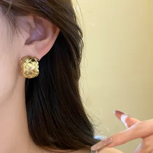 Vue détaillée d'une boucle d'oreille en C dorée avec une texture tressée élégante.