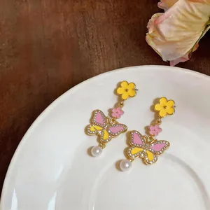 Close-up detail of vintage enamel butterfly earrings with yellow flowers and white pearl drops