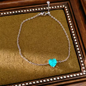 Close-up of a minimalist silver chain necklace featuring a teal green heart-shaped zircon.