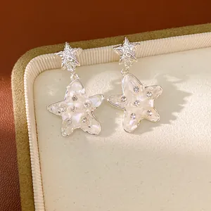 Dettaglio orecchini a stella con frammenti di conchiglia e strass su portagioie.