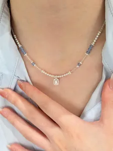 Detail of vacation-style necklace with white pearls, blue beads, and zircon pendant on model
