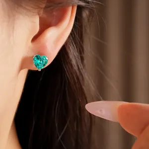 Close-up detail of a vibrant green heart-shaped zircon earring worn on a model's ear