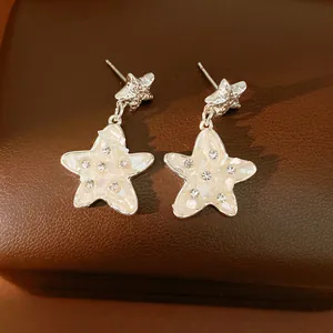 Vista dettagliata di orecchini a stella in argento con conchiglia e strass luminosi.
