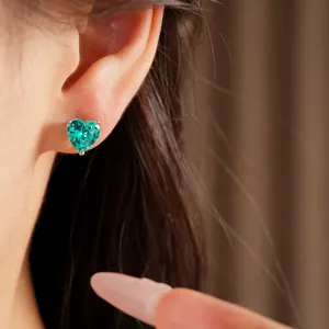 Close-up of a vibrant emerald green heart-shaped zircon stud earring worn on an ear