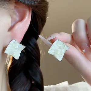 Detailed macro view of elegant silver rhombic stud earrings with shell inlay on ear