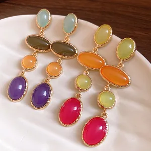 Close-up of vintage resin oval drop earrings with colorful stones in gold-tone setting.