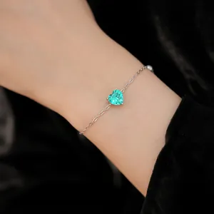 Close-up of a silver-toned bracelet featuring a heart-shaped emerald green zircon.