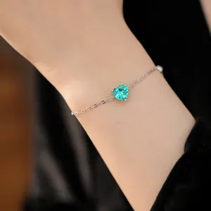 Close-up of a delicate silver chain bracelet with a heart-shaped green zircon gemstone