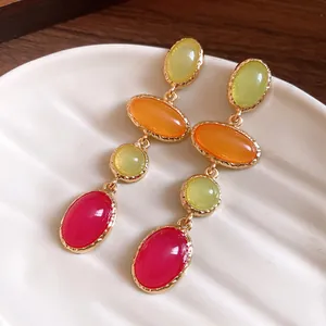 Macro view of colorful vintage resin oval drop earrings with green, orange, and red stones.
