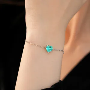 Detailed macro shot of a delicate silver chain bracelet with a green heart crystal
