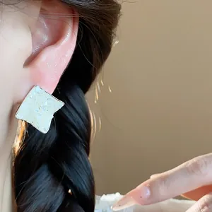 Close-up view of a minimalist rhombus mother-of-pearl earring with pleated silver metal edges