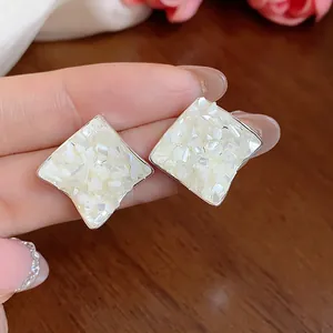 Macro view of minimalist rhombus stud earrings with crushed mother-of-pearl inlay details.