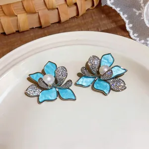 Close-up of blue floral stud earrings featuring cubic zirconia and central pearls.
