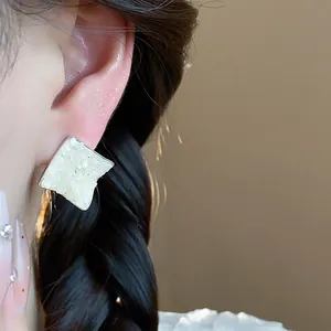 Close-up view of elegant rhombus stud earrings with crushed mother-of-pearl inlay worn on ear