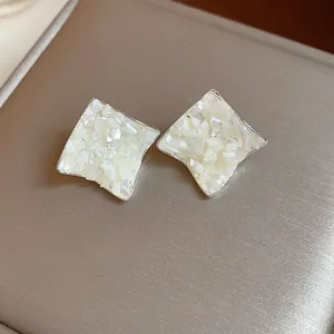 Close-up macro view of silver stud earrings featuring elegant white crushed shell inlay