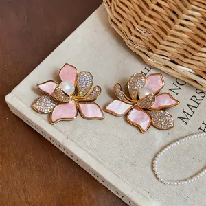 Close-up of elegant pink flower earrings with crystal zirconia and pearls on a vintage book.