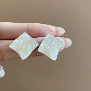 Elegant close-up of geometric rhombus stud earrings featuring crushed mother-of-pearl inlay