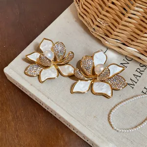 Detail of gold plated flower earrings with white shell petals and a pearl center