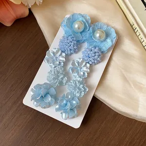 Elegantes pendientes azul claro con flores y perlas estilo dopamina en tarjeta blanca.