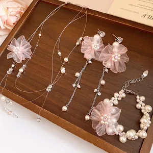 Détail de l'élégante parure de bijoux avec fleurs en mousseline rose et perles sur plateau bois