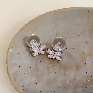 Nahaufnahme von Zirkon-Schmetterlings-Ohrsteckern mit Silbernadeln auf einem Keramikteller.